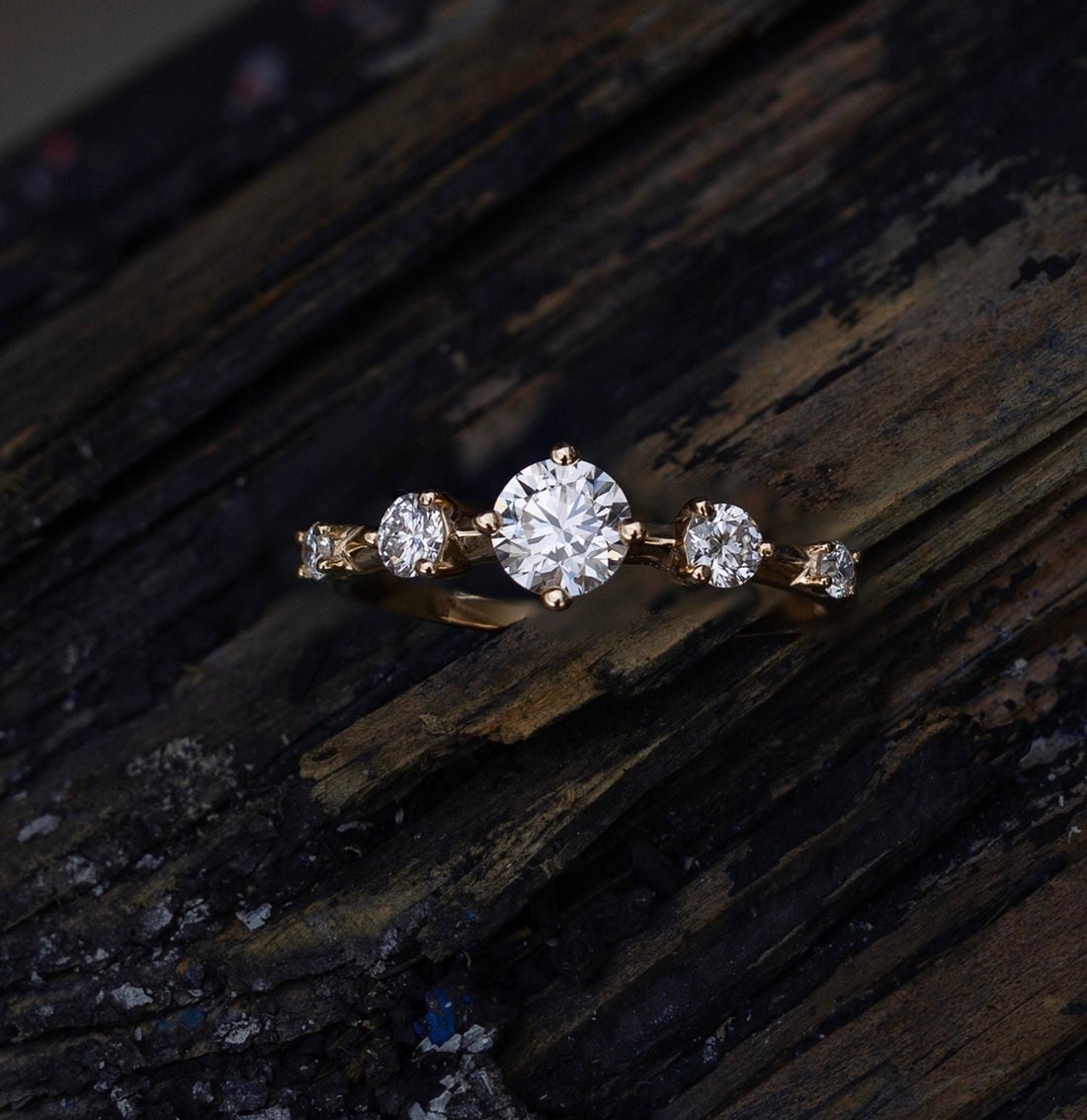 Round dainty five stone lab grown diamond wedding band in yellow gold on a dark wooden surface