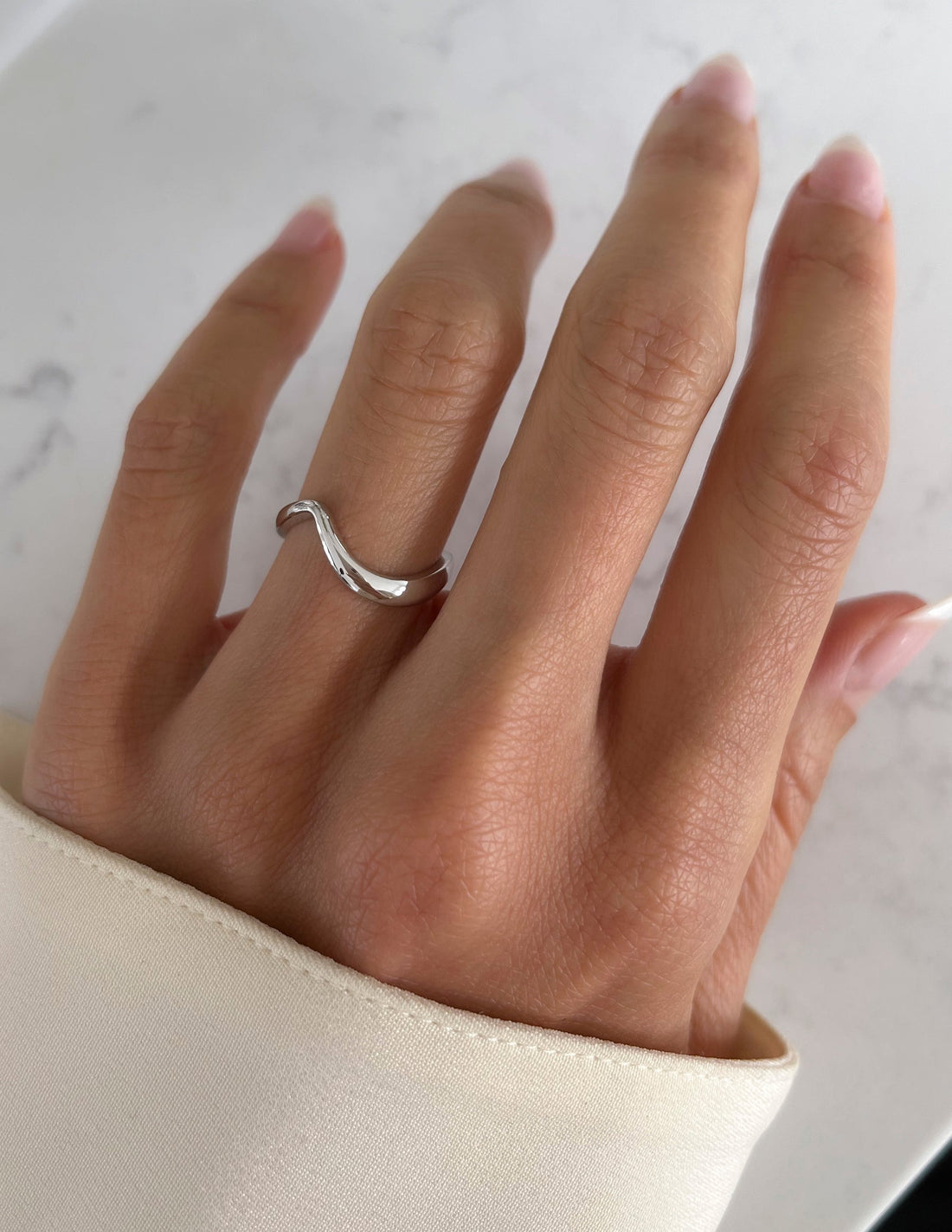 Polished plain contour wedding band in white metal worn on a hand