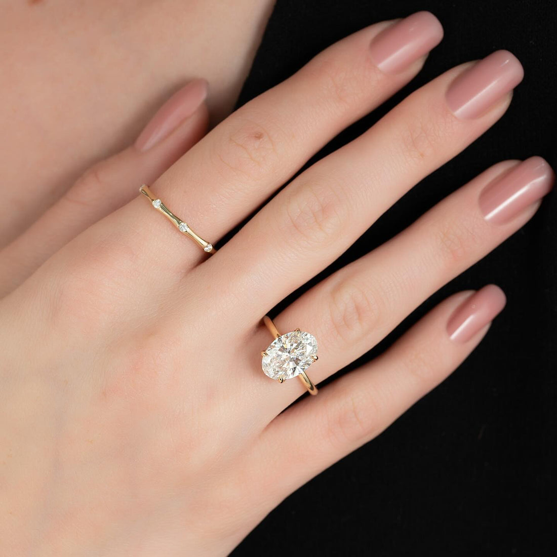 Oval cut lab grown diamond ring with tapered band and low profile basket in yellow gold worn on the hand