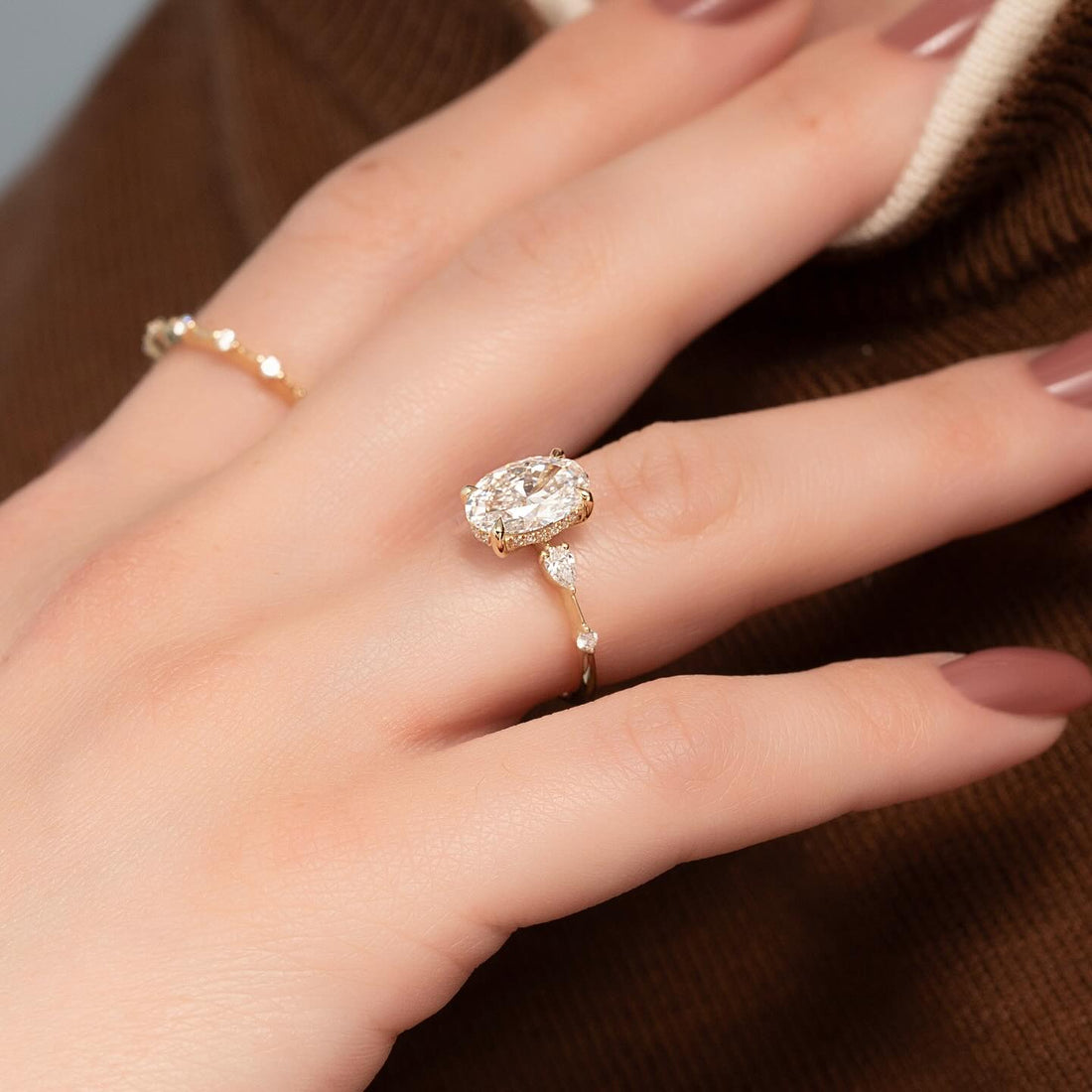 Oval cut lab grown diamond hidden halo ring with pear accent shoulders in yellow gold worn on the hand