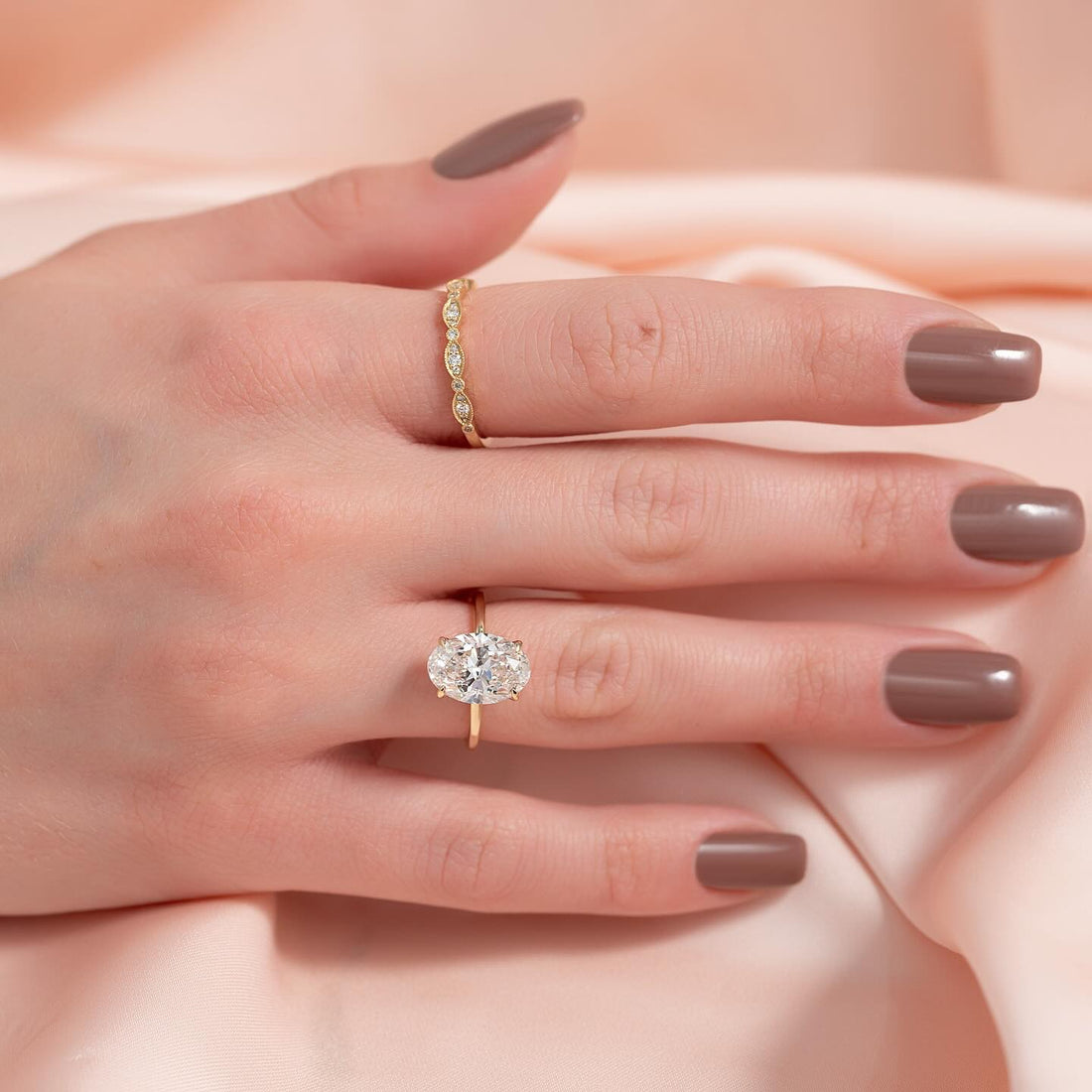 East west oval lab grown diamond solitaire ring on a thin yellow gold band worn on the hand