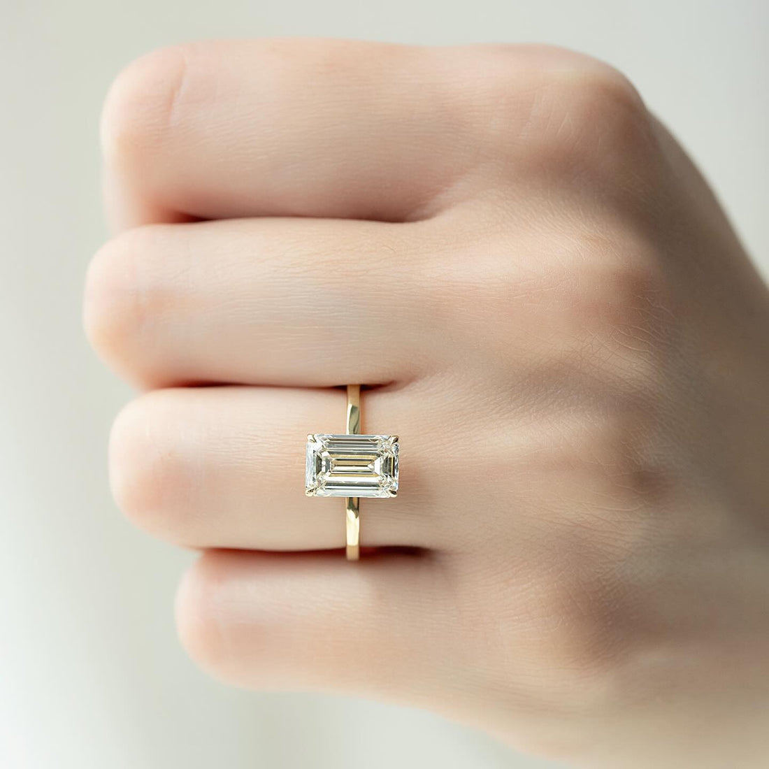 East west emerald cut lab grown diamond solitaire ring in yellow gold worn on the hand
