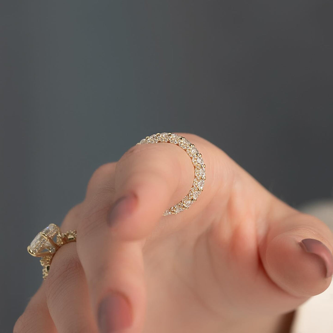 Round moissanite U-prong eternity band ring held in fingers in yellow gold