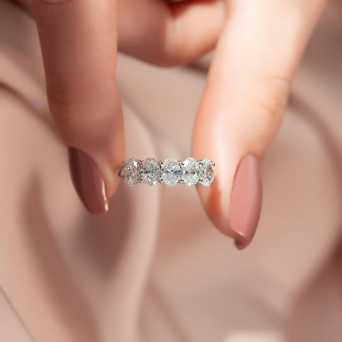 Oval moissanite five stone half eternity band ring held in fingers in white gold