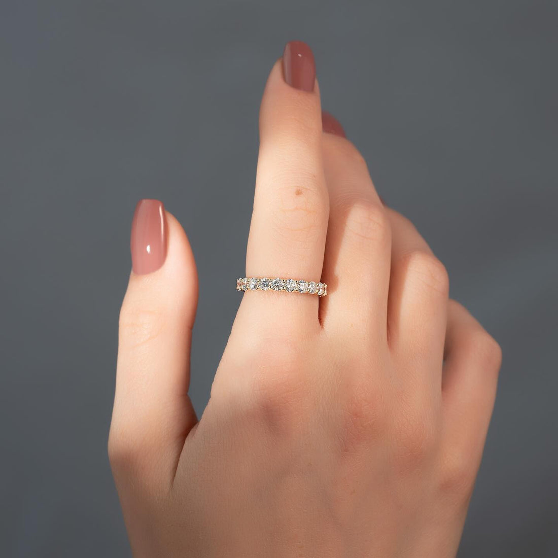 Round moissanite shared prong eternity band ring worn on hand in yellow gold