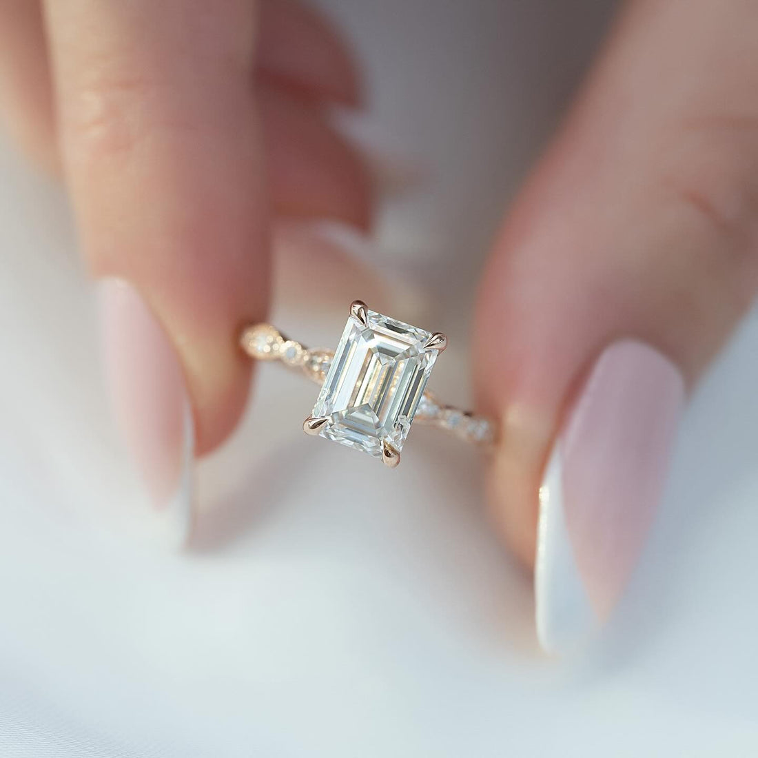 Emerald cut lab grown diamond ring in rose gold on a milgrain marquise station band