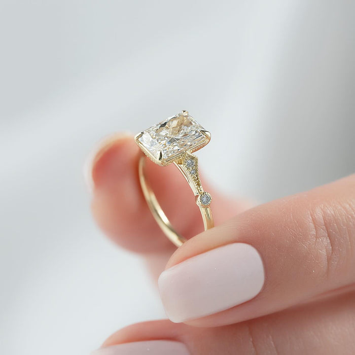 Radiant cut lab grown diamond ring in yellow gold with milgrain kite shoulders and a bezel station
