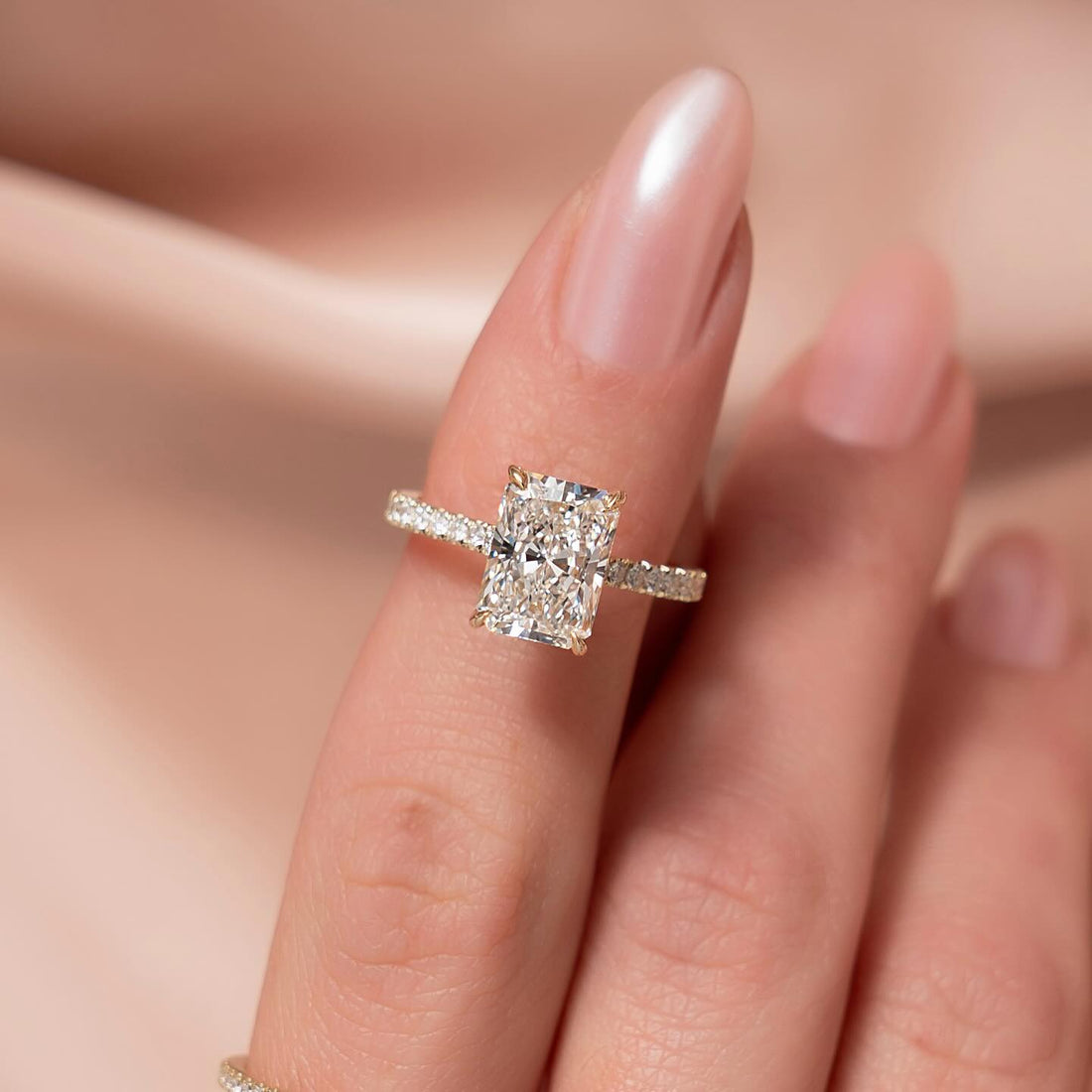 Elongated radiant cut lab grown diamond ring with three sided pave band in yellow gold worn on the hand