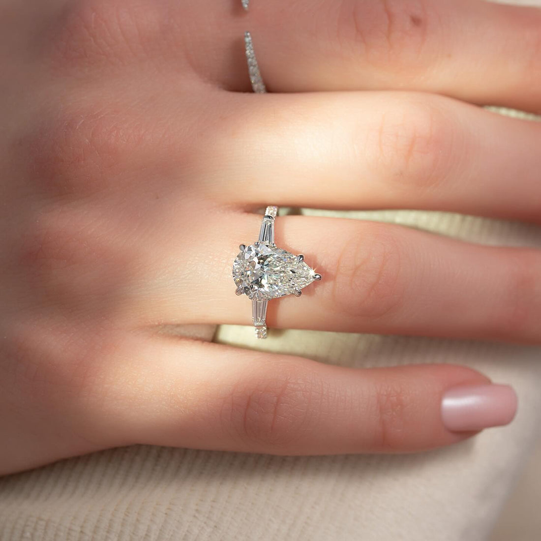 East west pear cut lab grown diamond ring with tapered baguette sides in white gold worn on the hand