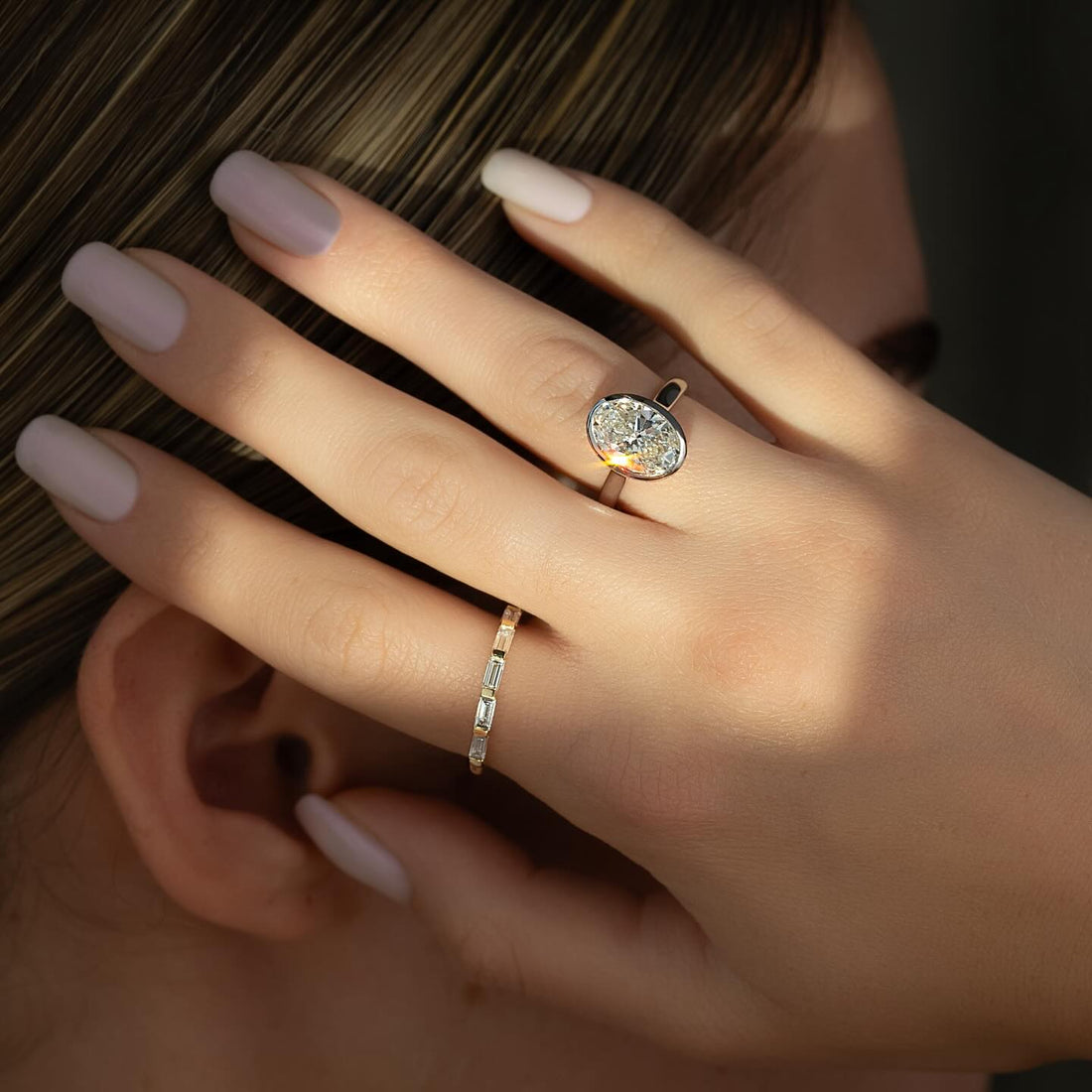 Bezel set oval lab grown diamond ring with fine rim in rose gold worn on hand