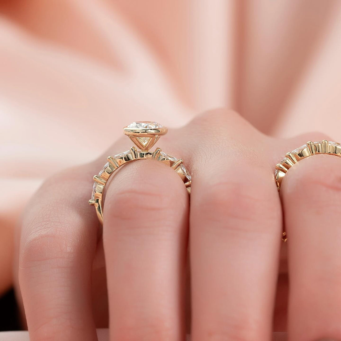 Round moissanite bezel marquise accent band ring on hand in yellow gold