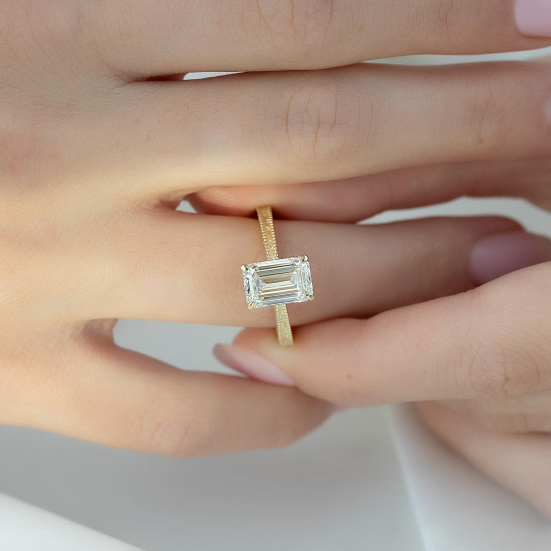 East west emerald cut lab grown diamond ring on a hand engraved milgrain yellow gold band