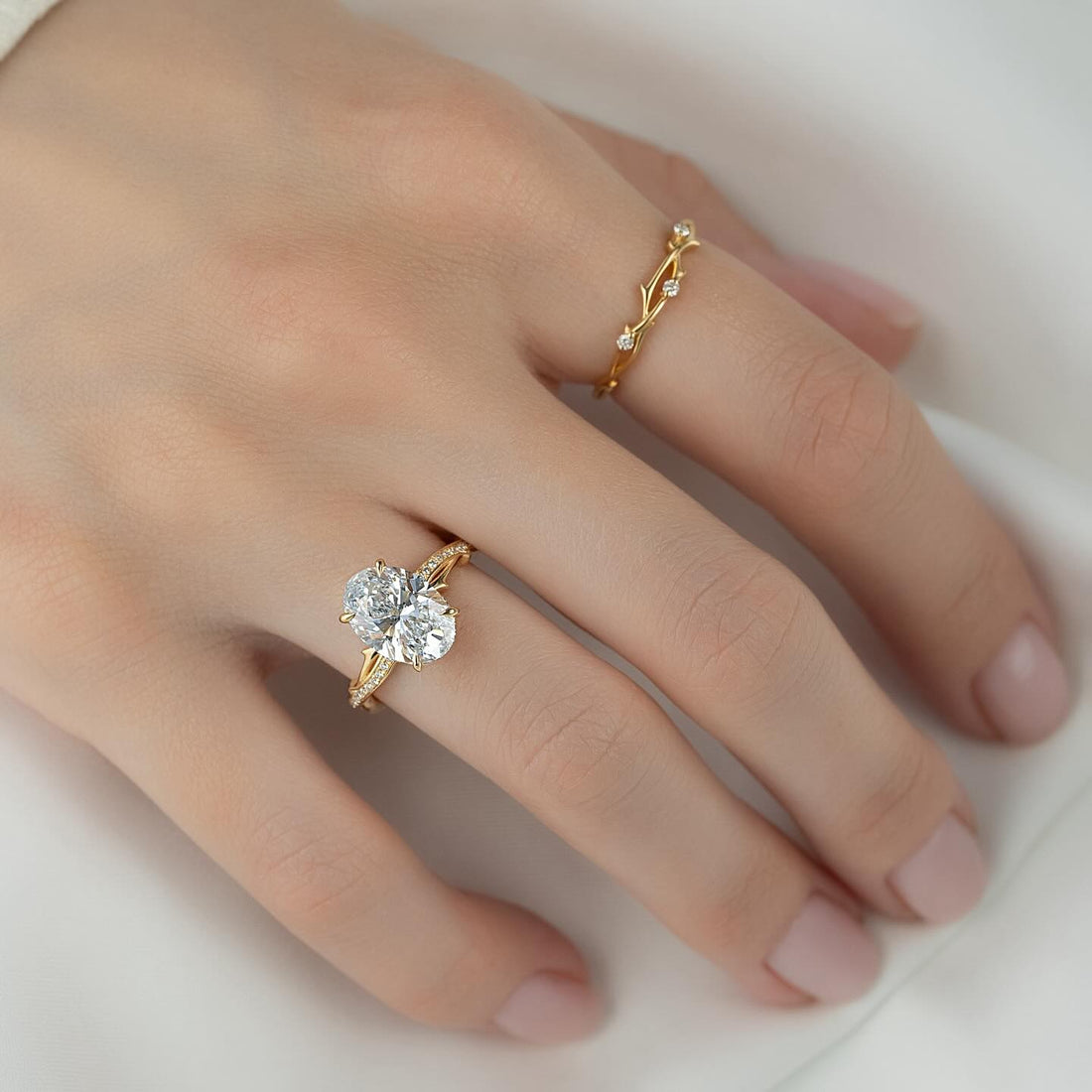 Oval lab grown diamond ring on a pave branch band in yellow gold worn on hand