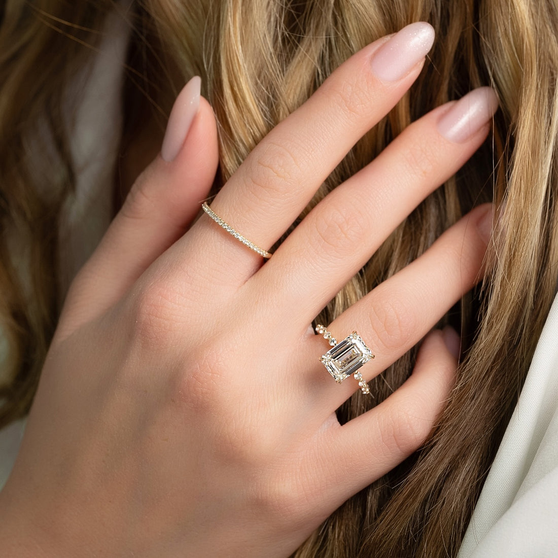 Emerald cut lab grown diamond ring with hidden halo and graduated round band in yellow gold worn on the hand