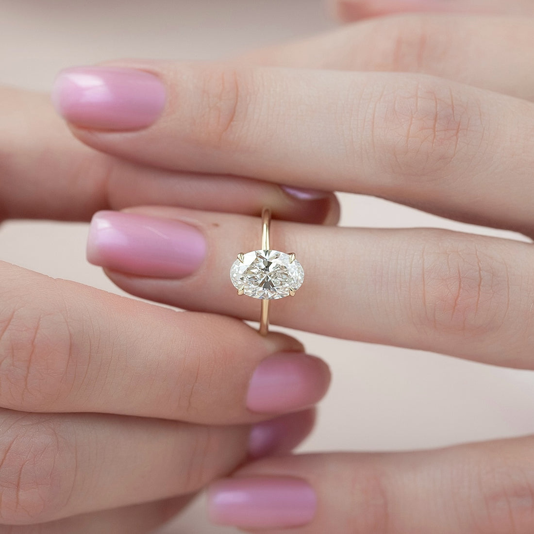 East west oval cut lab grown diamond ring on a fine wire yellow gold band worn on the hand
