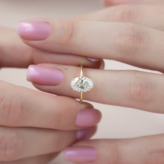 East west oval cut lab grown diamond ring on a fine wire yellow gold band worn on the hand