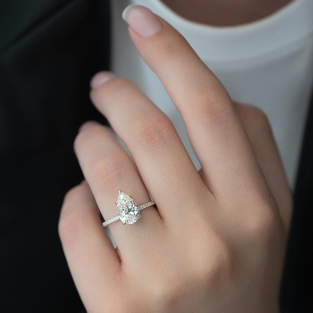 Pear cut lab grown diamond solitaire ring in white gold with a pave shank worn on the hand