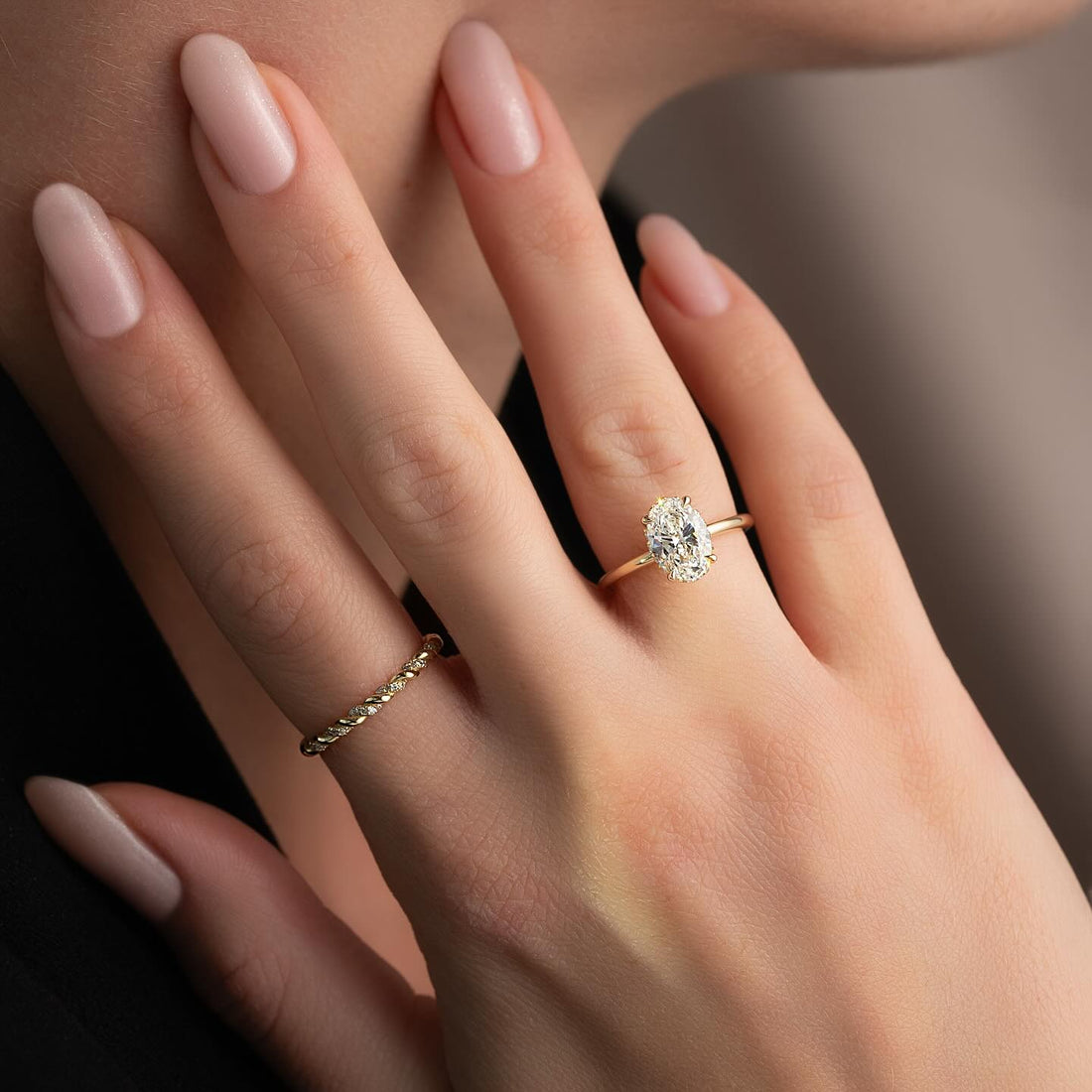 Oval cut lab grown diamond ring with hidden halo on a plain slim yellow gold band worn on the hand