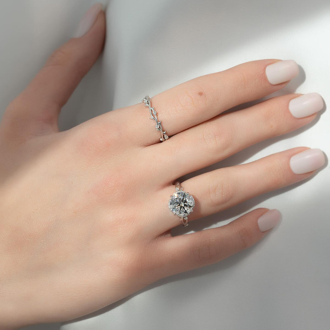 Round cut lab grown diamond halo ring with vine leaf band in white gold worn on the hand