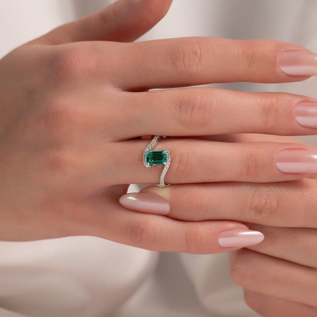 East west emerald cut emerald ring with bypass pave diamond band in white gold worn on the hand