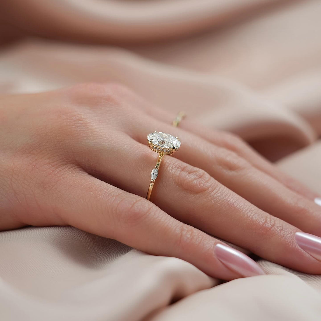 Oval cut lab grown diamond ring with hidden halo and single marquise shoulders in yellow gold worn on the hand