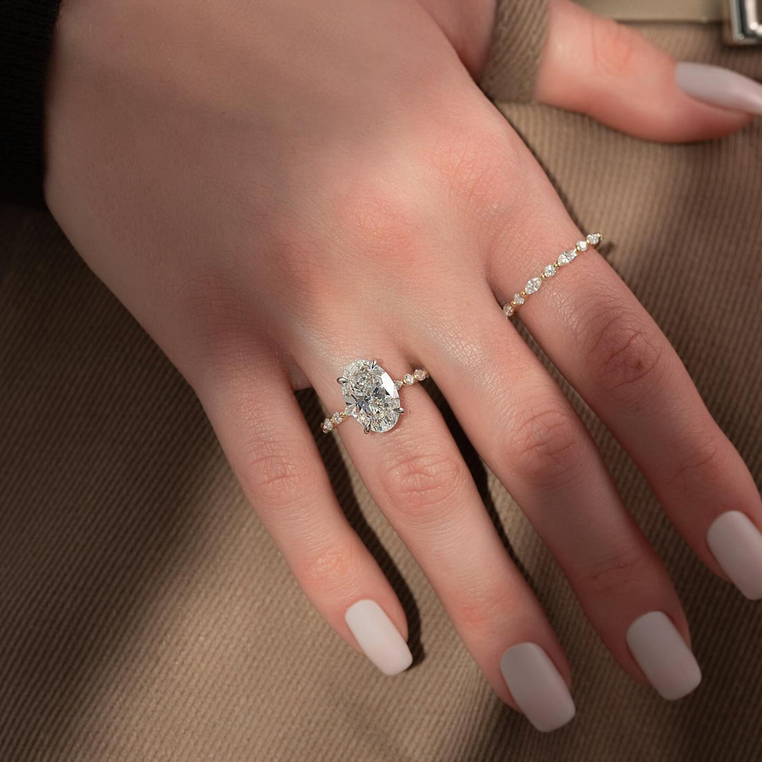 Oval cut lab grown diamond ring with tapering accent band in yellow gold worn on the hand