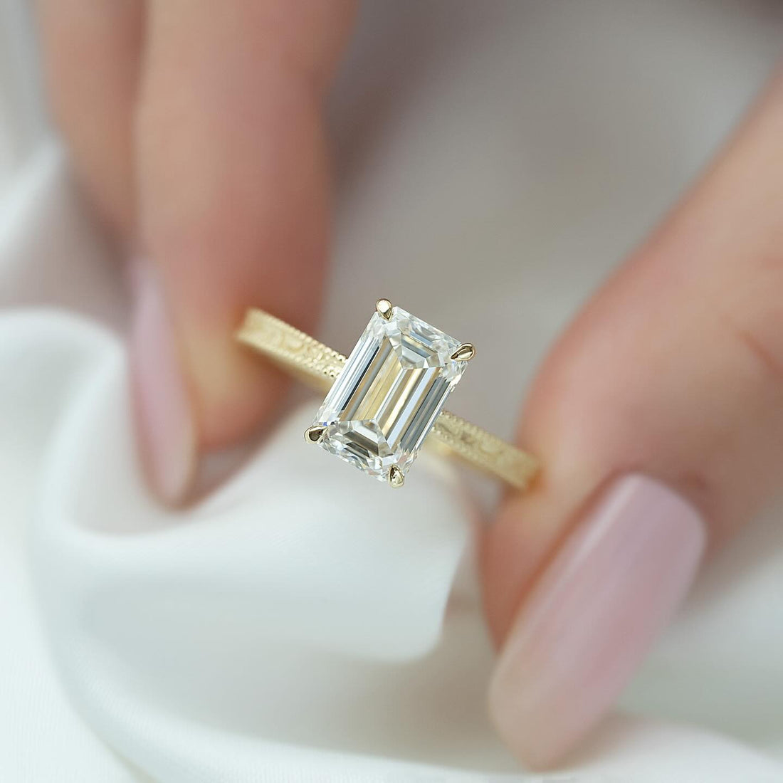 Emerald cut lab grown diamond solitaire ring on a flat engraved yellow gold band