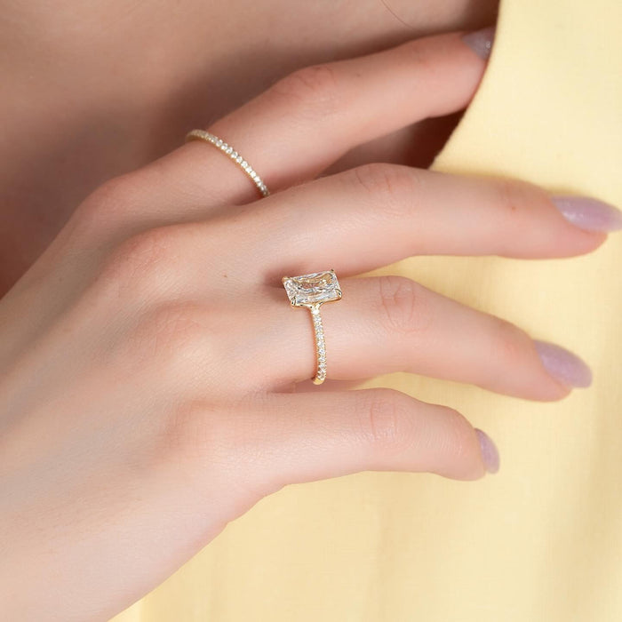 Elongated radiant cut lab grown diamond ring with pave shoulders in yellow gold worn on the hand