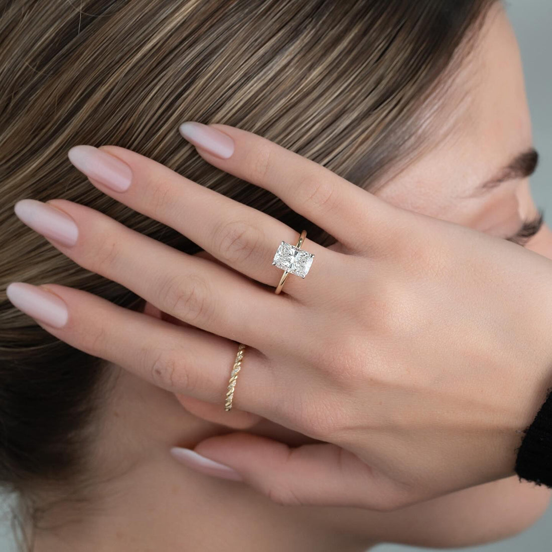 Elongated radiant cut lab grown diamond solitaire ring on a plain yellow gold band worn on the hand