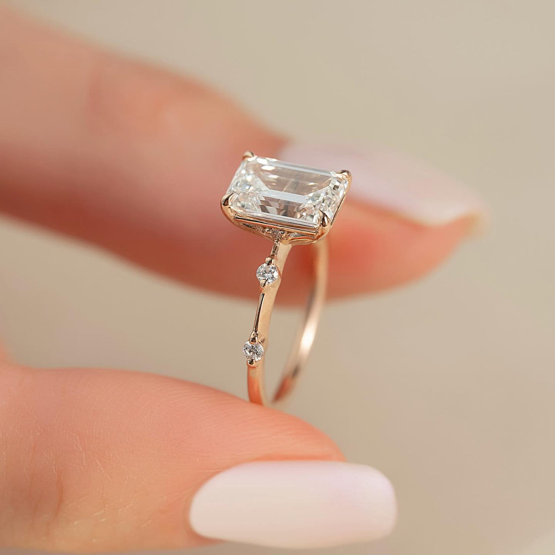 Emerald cut lab grown diamond ring with spaced round accents on a thin rose gold shank