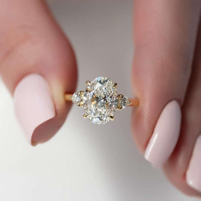 Oval cut lab grown diamond three stone ring in yellow gold with round side stones