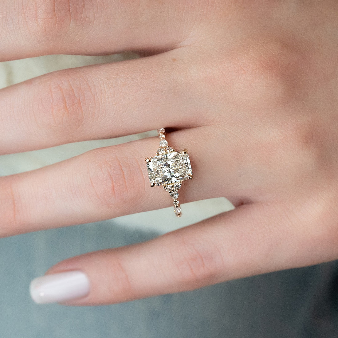 East west radiant lab grown diamond ring with graduated cluster shoulders worn on hand