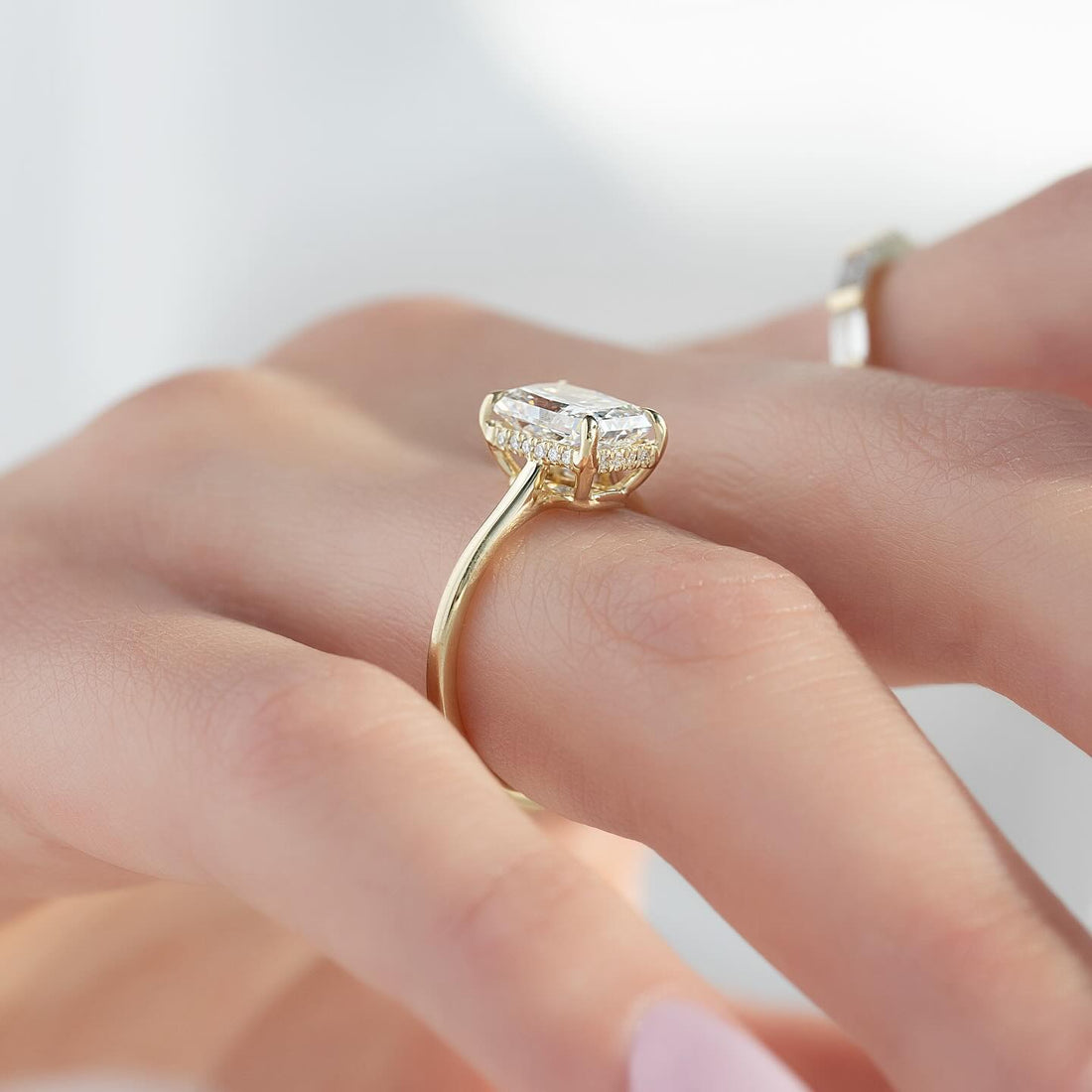 Elongated radiant cut lab grown diamond ring in yellow gold with a full concealed halo on a bare shank