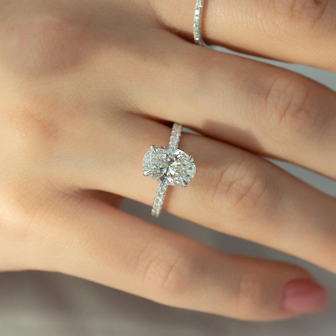 Oval cut lab grown diamond solitaire ring on a slim pave white gold shank worn on the hand