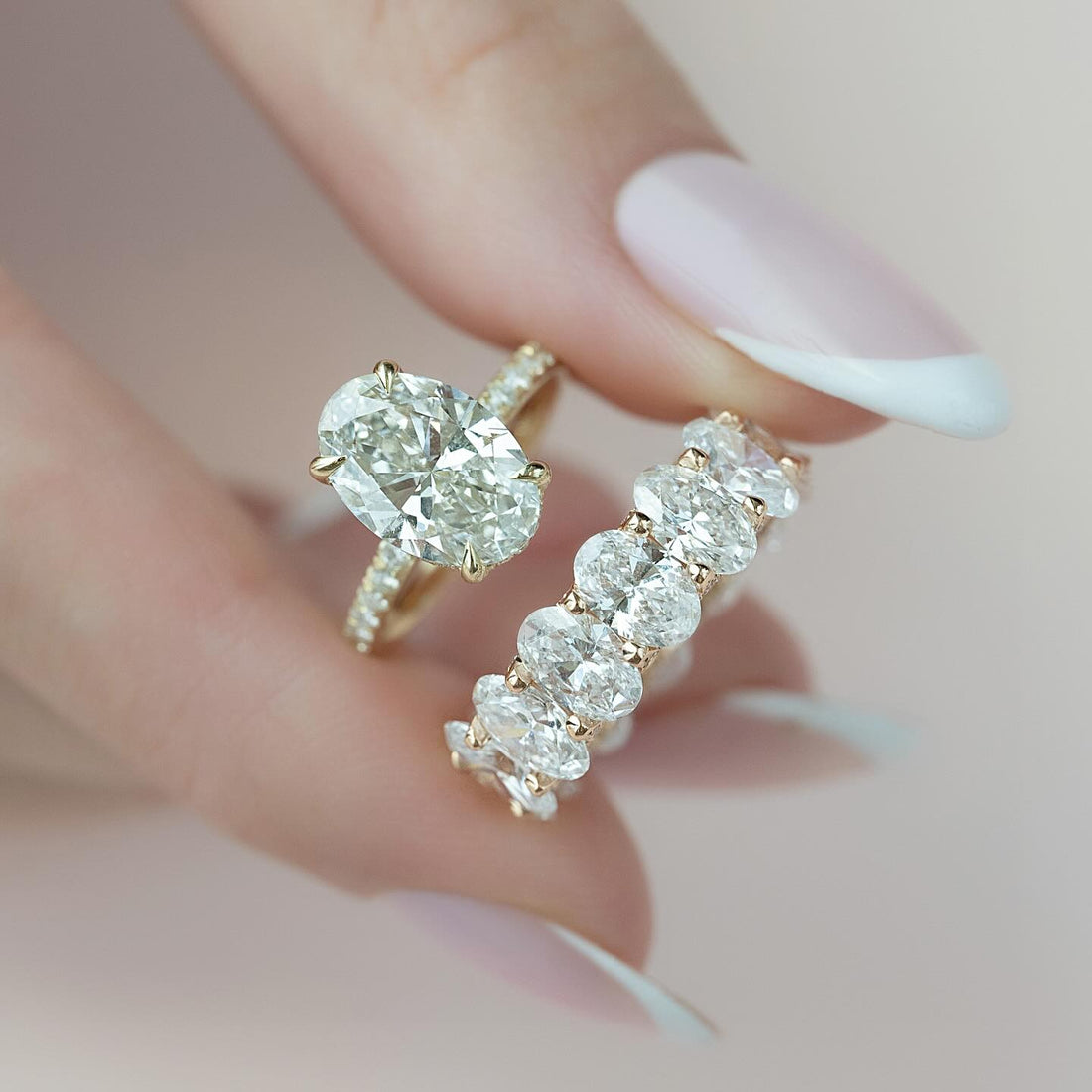 Oval lab grown diamond engagement ring with a pave shank beside an oval cut eternity band in yellow gold