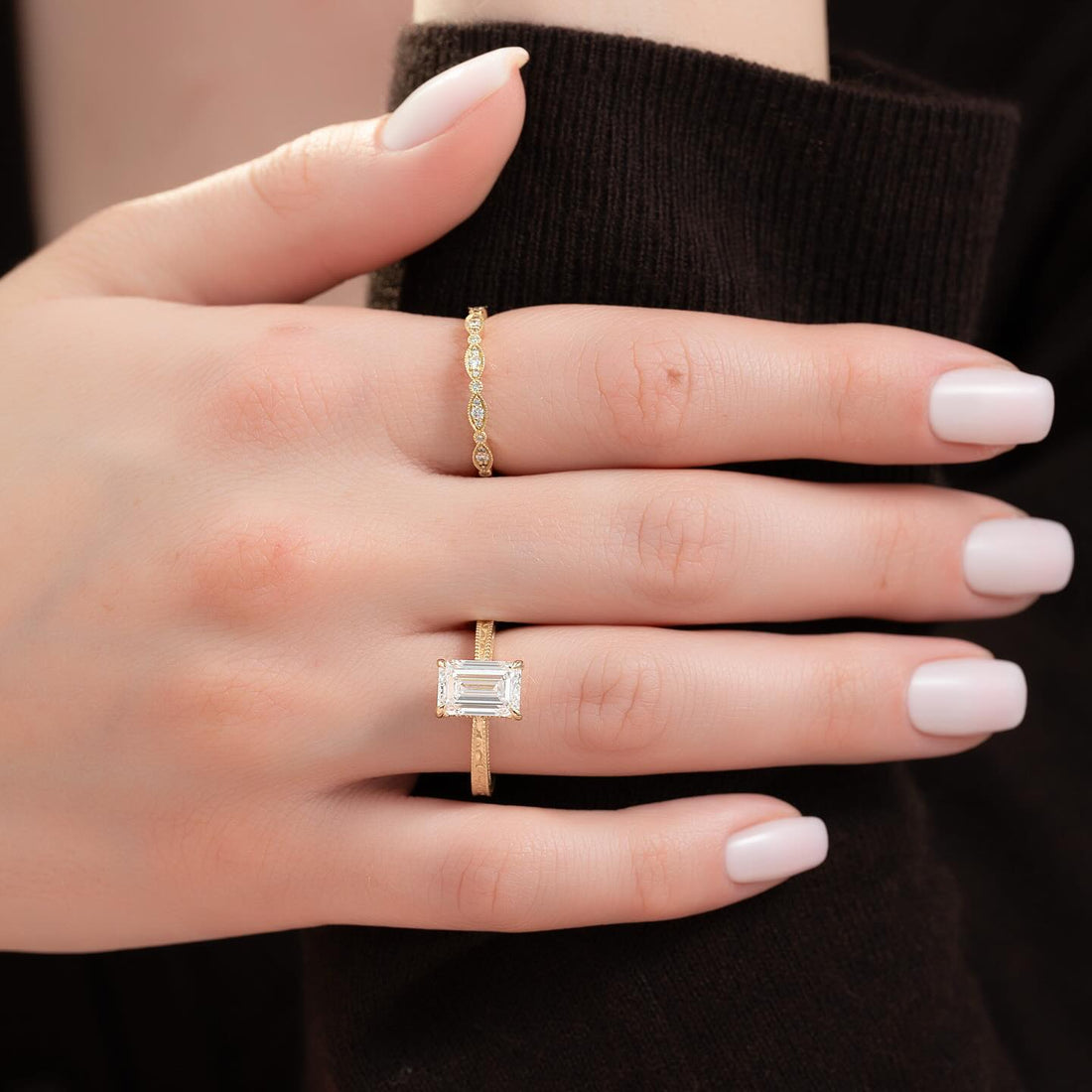 Emerald cut lab grown diamond solitaire with milgrain edged band in yellow gold worn on the hand