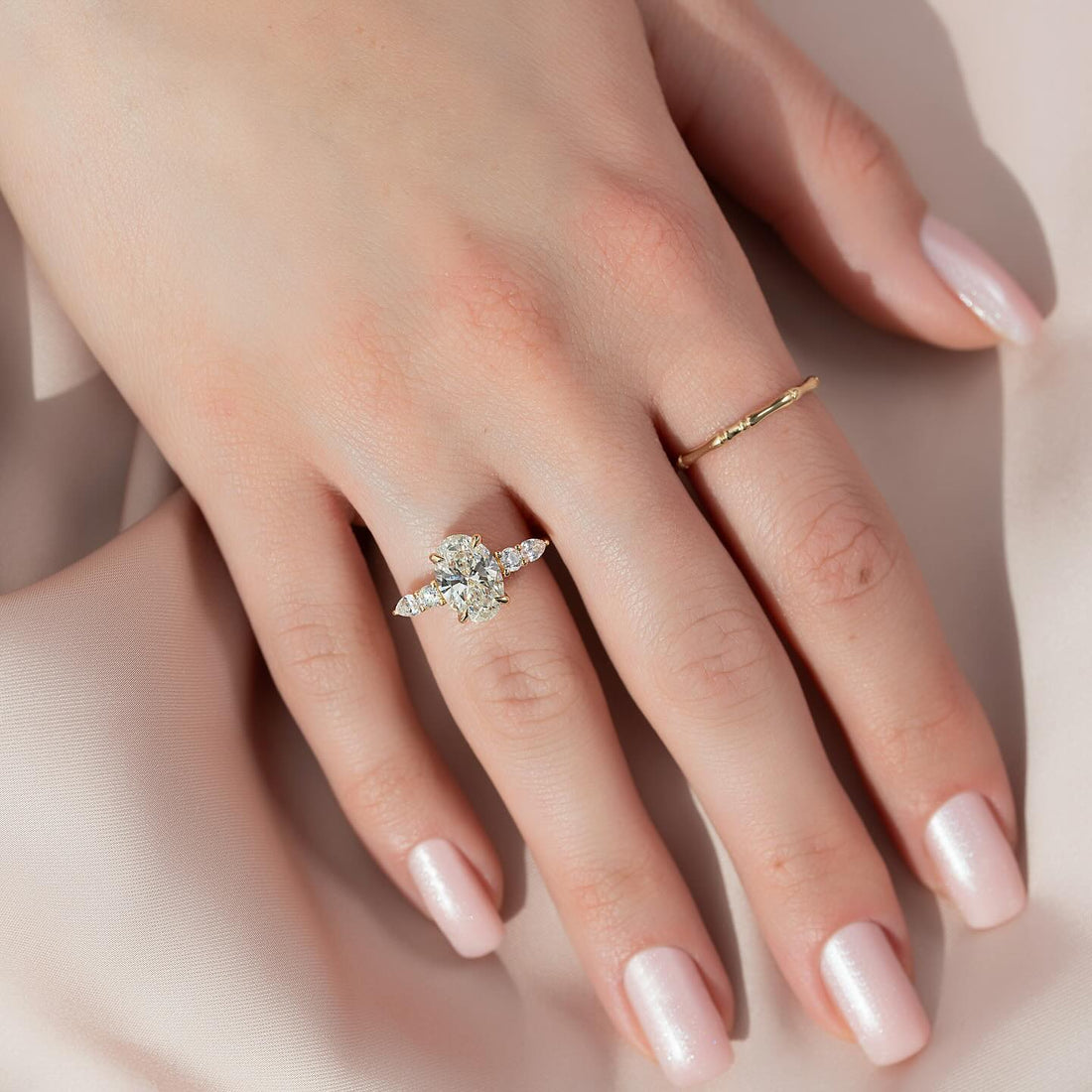 Oval cut lab grown diamond three stone ring with pear side stones in yellow gold worn on the hand