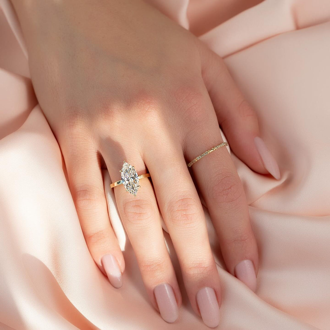 Marquise cut lab grown diamond solitaire ring on a flat plain yellow gold band worn on the hand