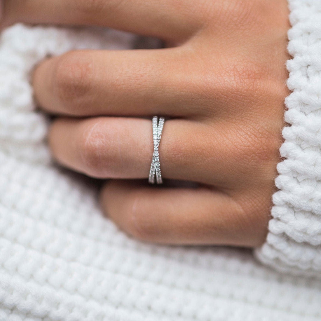 Round moissanite cross over pave wedding band in white gold worn on a finger