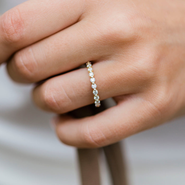 Round moissanite bubble prong wedding band in yellow gold worn on a finger