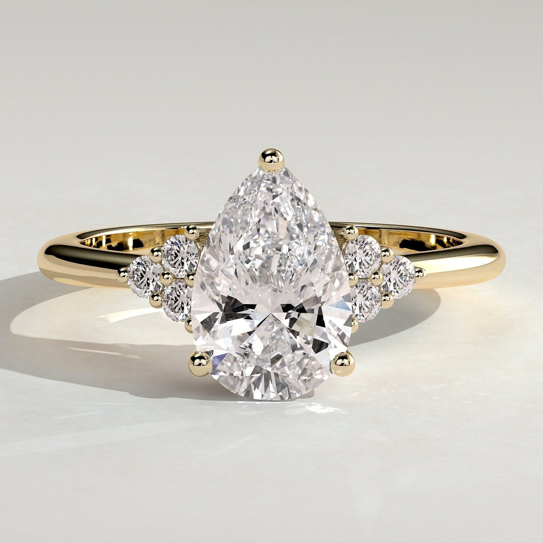 Pear cut lab grown diamond ring with accent trios at the shoulders in yellow gold
