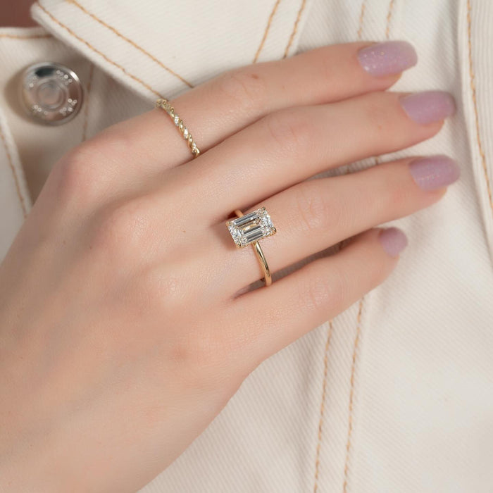 Emerald cut lab grown diamond hidden halo solitaire ring in yellow gold worn on the hand