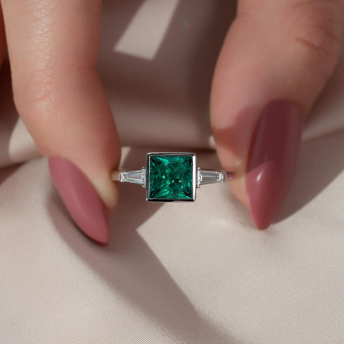 Square cut lab grown emerald bezel ring with tapered baguette diamond sides in white gold