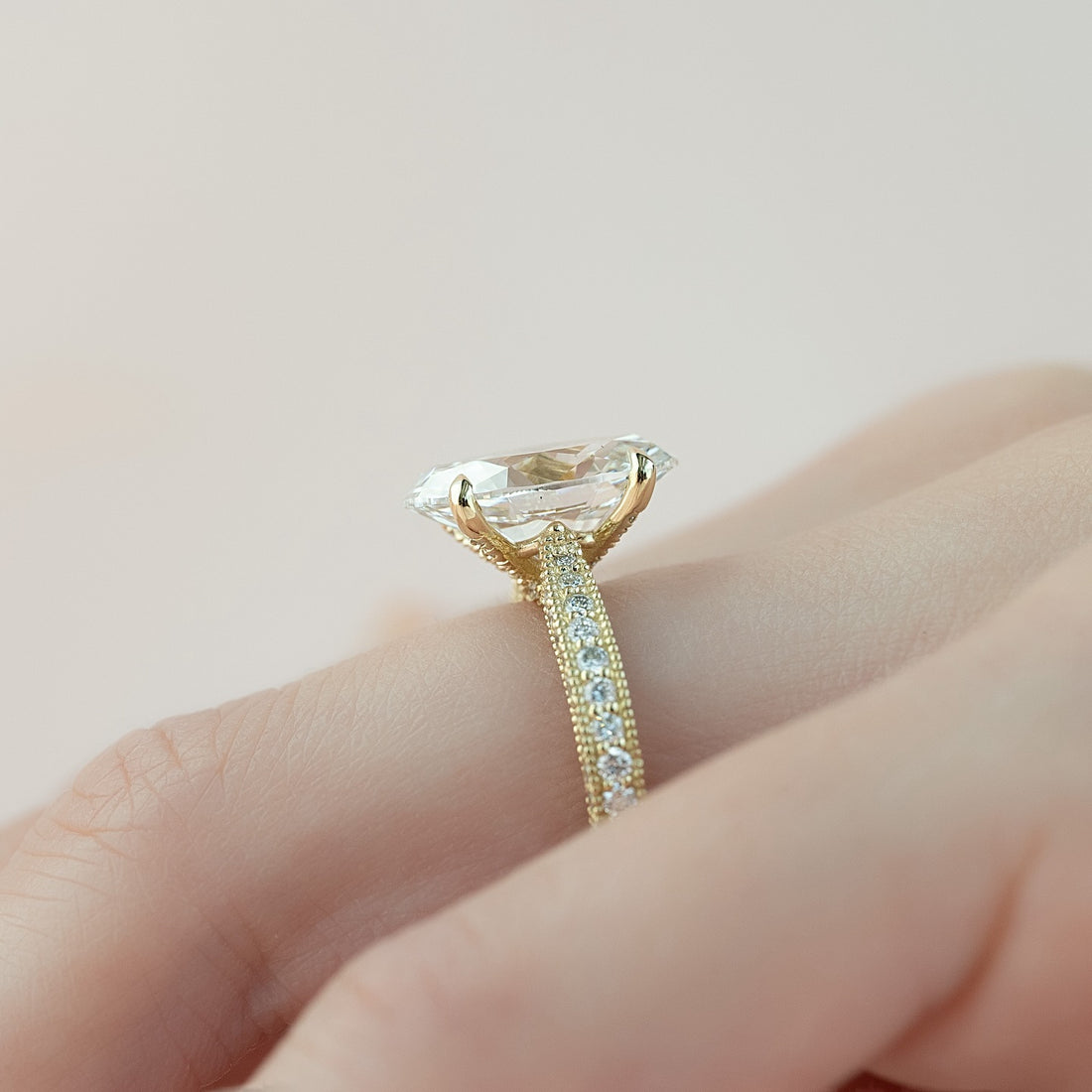 Profile of an oval cut lab grown diamond ring in yellow gold with a tall six claw head and milgrain edged pave band