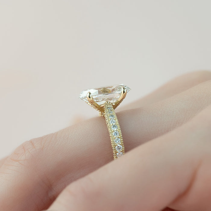 Profile of an oval cut lab grown diamond ring in yellow gold with a tall six claw head and milgrain edged pave band