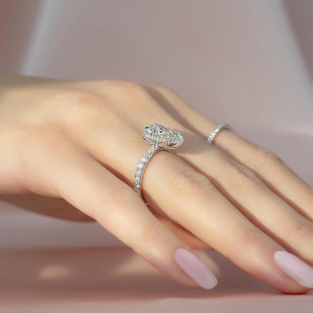 Oval cut lab grown diamond ring with hidden halo and split claws on a pave white gold band