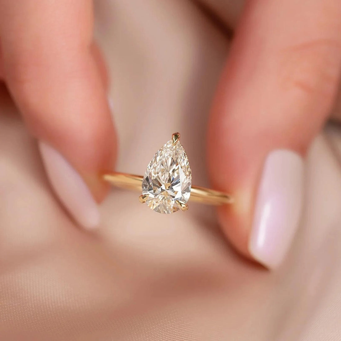 Pear cut lab grown diamond solitaire engagement ring in yellow gold held between fingers