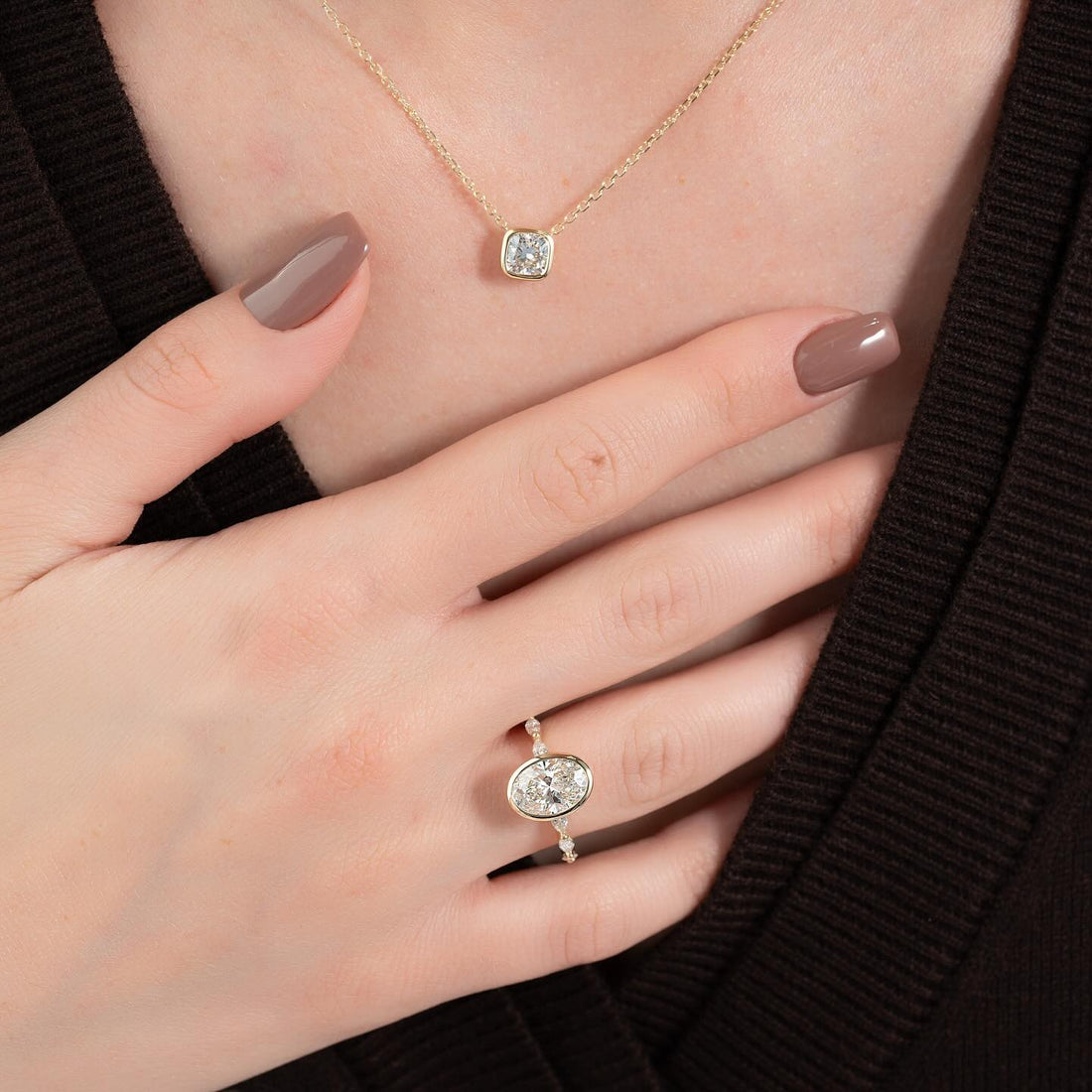 East west oval lab grown diamond bezel ring with marquise station band in yellow gold worn on the hand