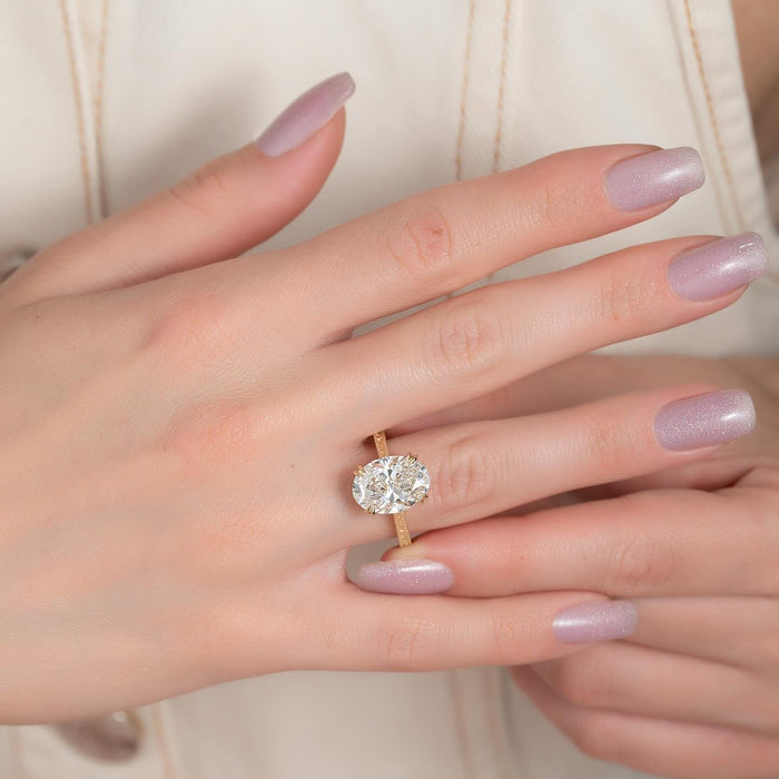 Oval cut lab grown diamond ring with engraved scroll band in yellow gold worn on the hand