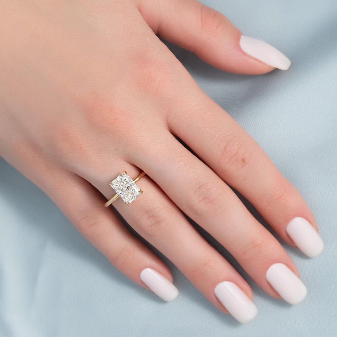 Elongated radiant cut lab grown diamond plain band solitaire in yellow gold worn on the hand